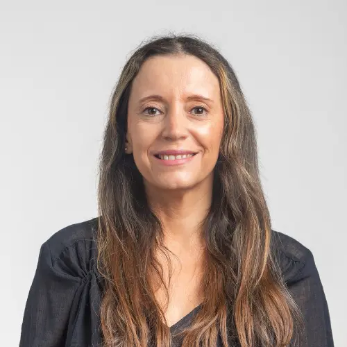Smiling woman with long brown hair wearing a dark top, posed against a light gray background.