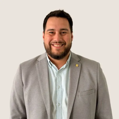 Smiling man with short dark hair and beard in a light gray blazer and pale blue shirt, posing for a professional headshot.