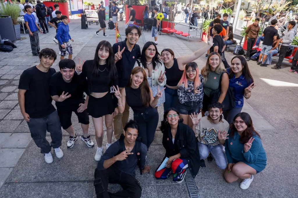 Group of diverse friends posing for a selfie at an outdoor event, smiling and flashing peace signs.