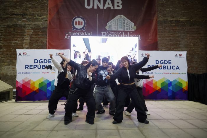 Group of students performing a dance routine on a stage with banners in the background at a university event.