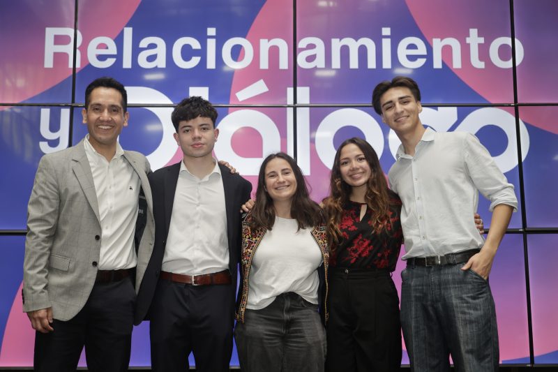 Five people (three men and two women) smiling and posing in front of a colorful backdrop that says 'Relacionamiento'.