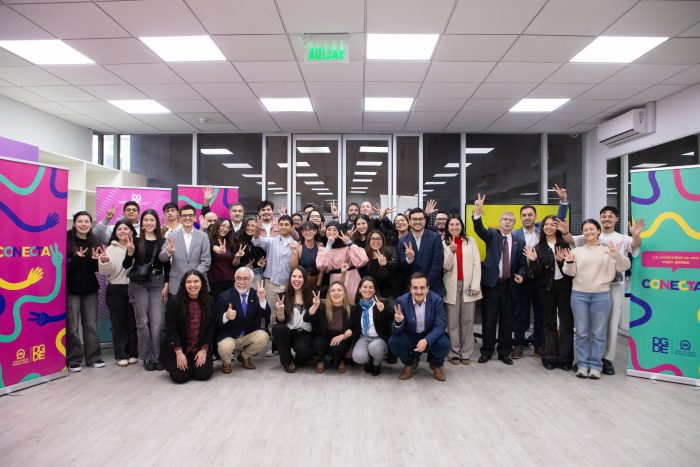 Diverse group of around 40 professionals posing for a group photo in an office with bright banners reading CONECTA on either side.